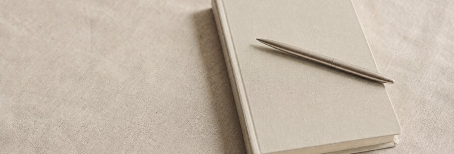 Ein geschlossenes Notizbuch mit einem Stift darauf, auf hellem Leinen.